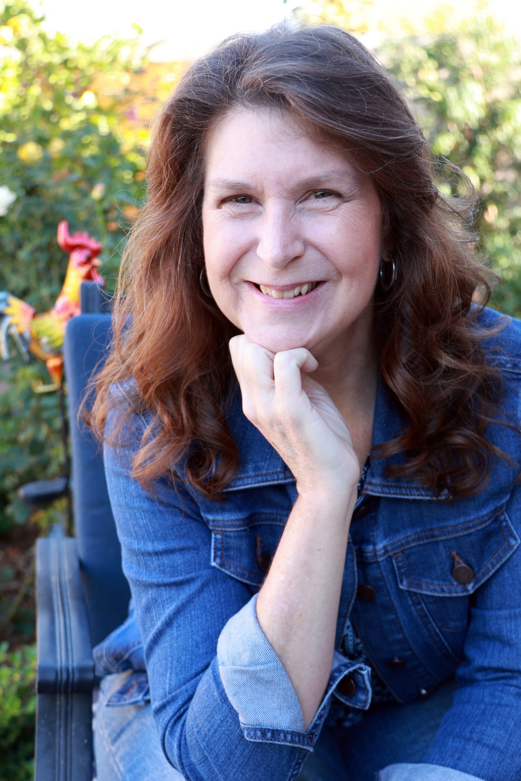 Denise M. Colby sitting outside with a rooster in the background to represent Bert a character in her books When Plans Go Awry, A Slight Change of Plans, A Whole New Plan